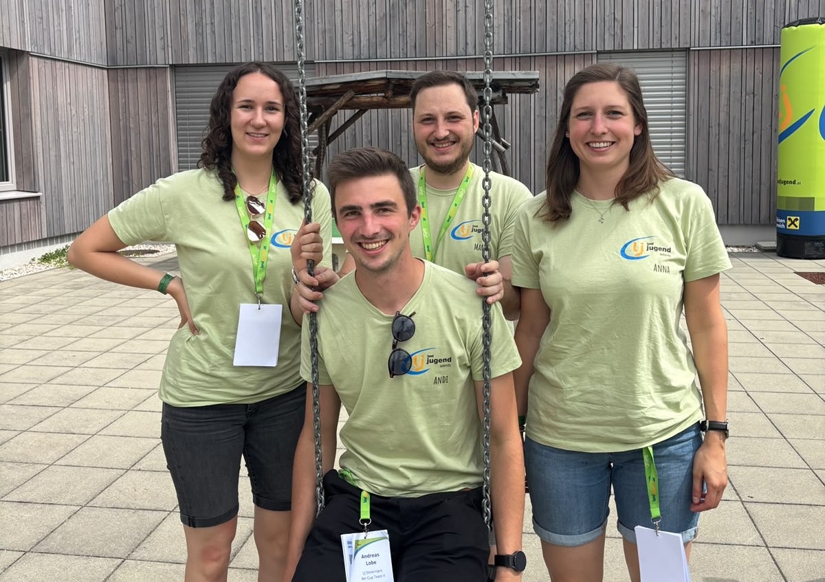 Vier junge Leute in hellgrünen T-Shirts stehen vor einer Holzwand.