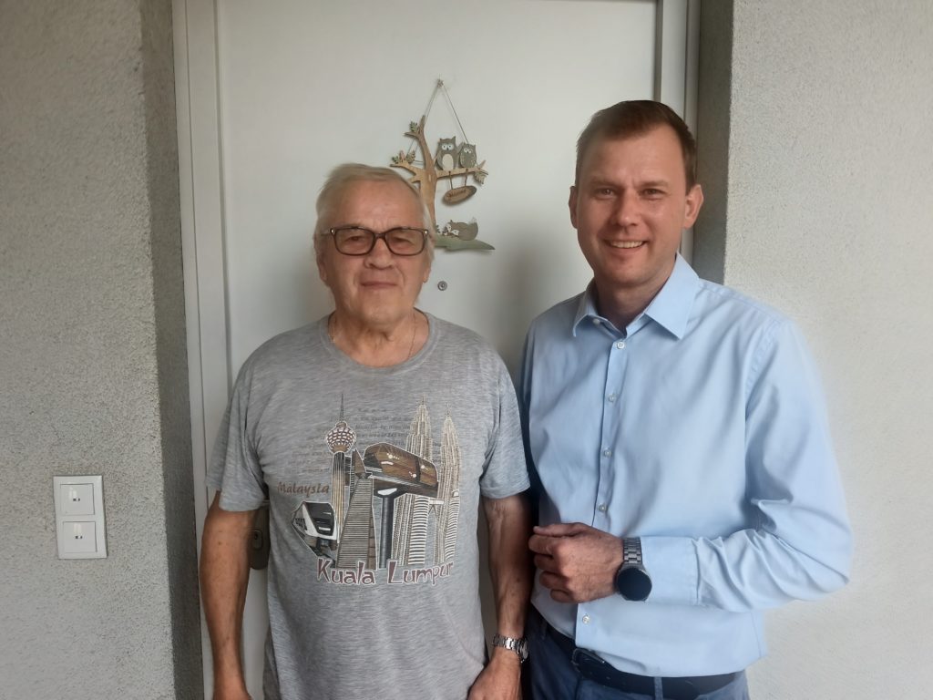 Zwei Männer vor einer Tür, einer mit Brille und T-Shirt mit Kuala Lumpur Aufdruck.