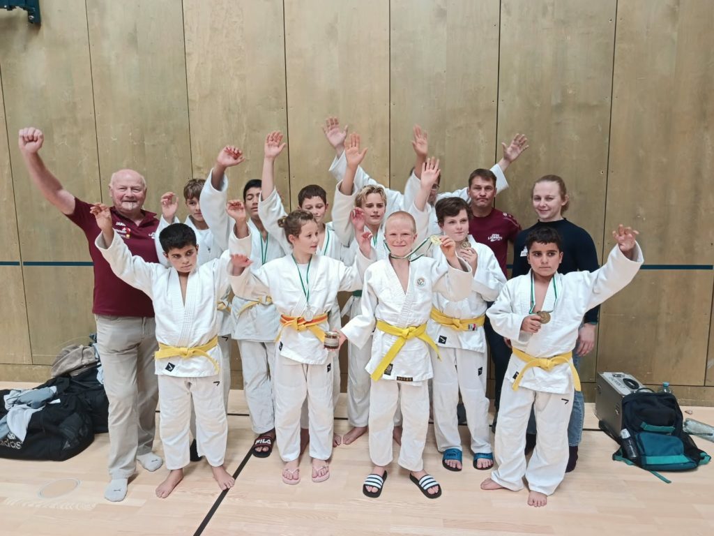 Judoka mit Medaillen und Betreuer jubeln in einer Turnhalle.